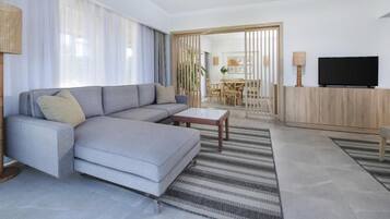 A modern living room with a grey sectional sofa, a coffee table, a TV, and a dining area in the background.