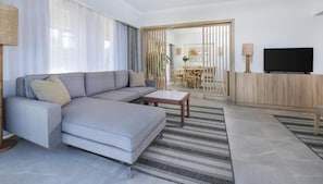 Una sala de estar moderna con un sofá seccional gris, una mesa de centro, un televisor y un área de comedor al fondo.