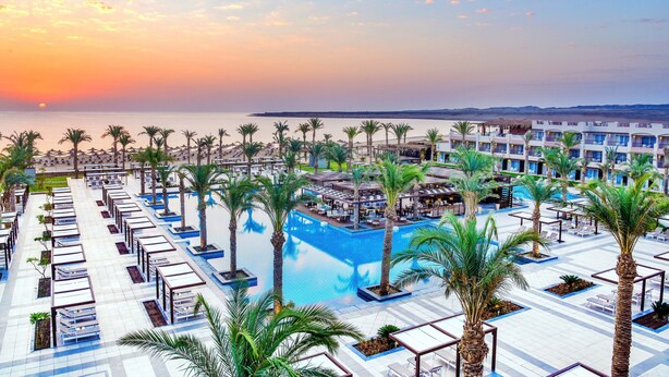 Un resort con una piscina grande, tumbonas y palmeras.