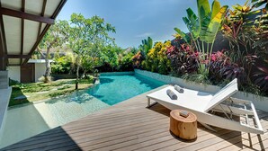 A wooden deck with a pool, lounge chairs, and tropical plants.
