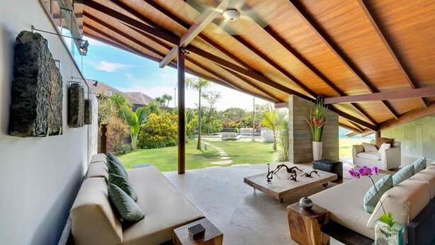 A spacious living area with a high ceiling, a stone wall, and a view of a lush garden.