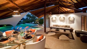 Un espace extérieur aménagé pour les repas, avec une table en verre, des sièges confortables et une piscine en arrière-plan.