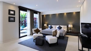 Ein modernes Hotelzimmer mit einem großen Bett, zwei Nachttischen mit Lampen, einem Flachbildfernseher, einer Sitzecke mit Sofa und Hocker sowie einem Balkon mit Vorhängen.