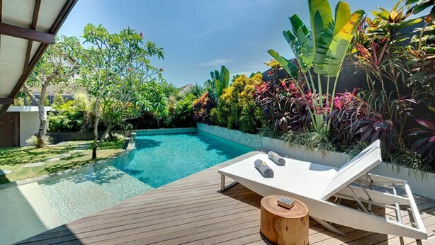Ein Pool mit Holzterrasse, Liegestühlen und tropischen Pflanzen.