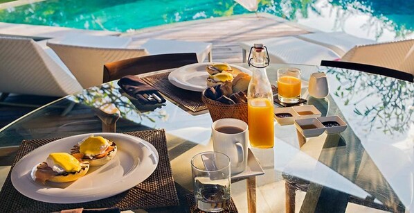 A breakfast setting with a glass table, plates of food, a coffee cup, a glass of orange juice, and a bottle of water.