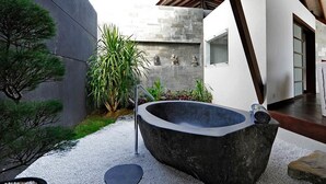 Ein moderner Wellnessbereich im Freien mit einem Steintonne, einem kleinen Garten mit Pflanzen und einem Weg.