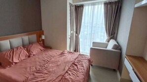 Un dormitorio con cama, una silla y una ventana con cortinas.