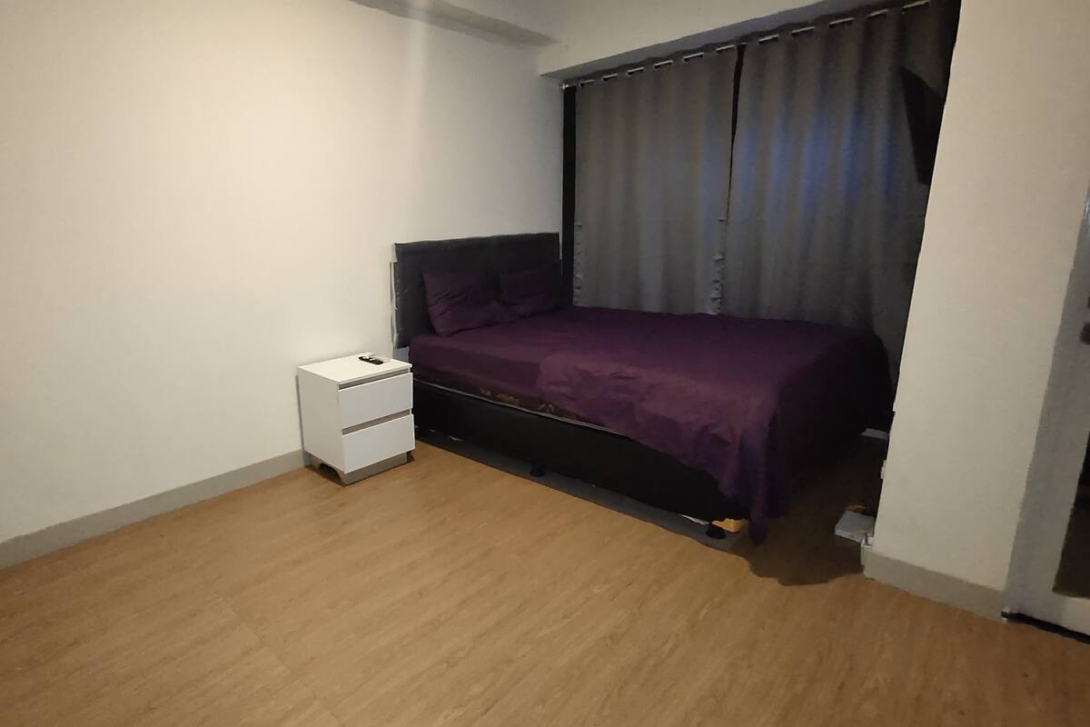 A bedroom with a bed, a nightstand, and a window with curtains.