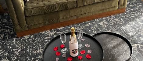 A green sofa with floral cushions, a bottle of champagne, and rose petals on a black table.