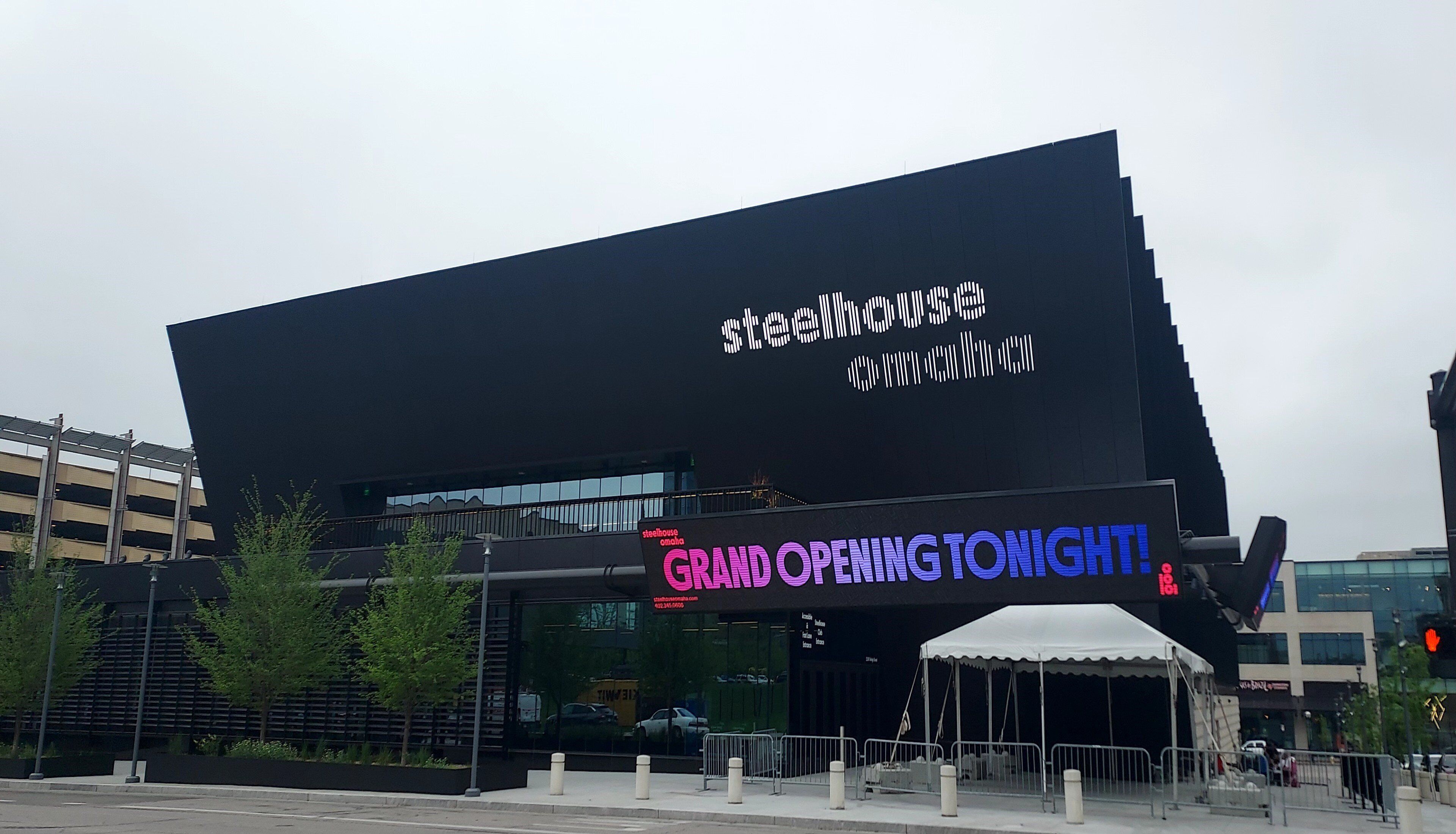Un edificio moderno con un grande display digitale che annuncia una grande inaugurazione stasera.