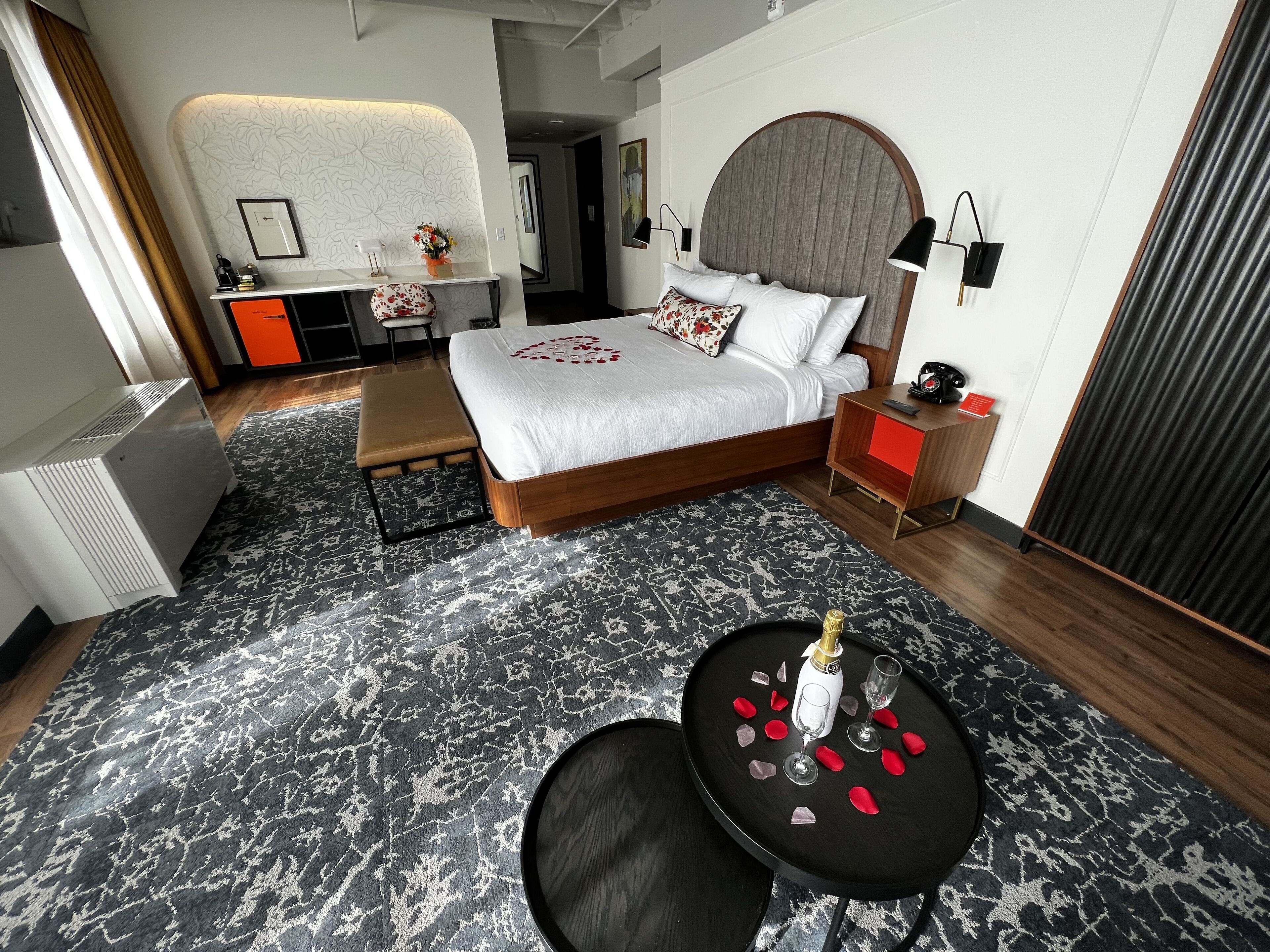 A modern hotel room with a large bed, bedside tables, a desk, and a small seating area.