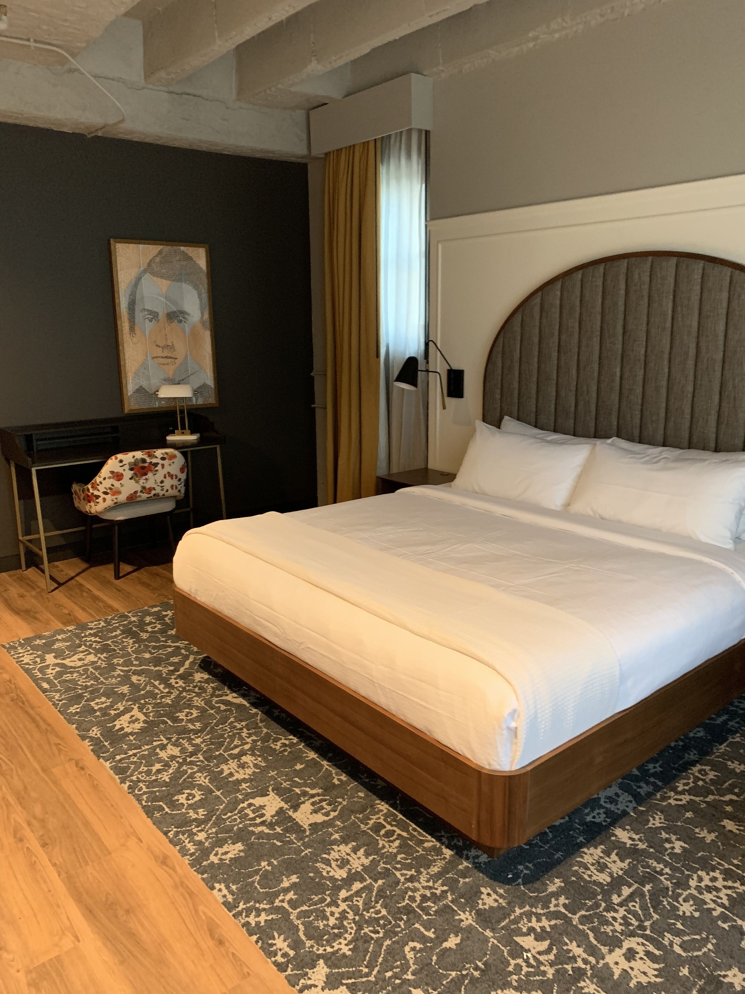 A hotel room with a large bed, a desk, a chair, a lamp, and a painting on the wall.