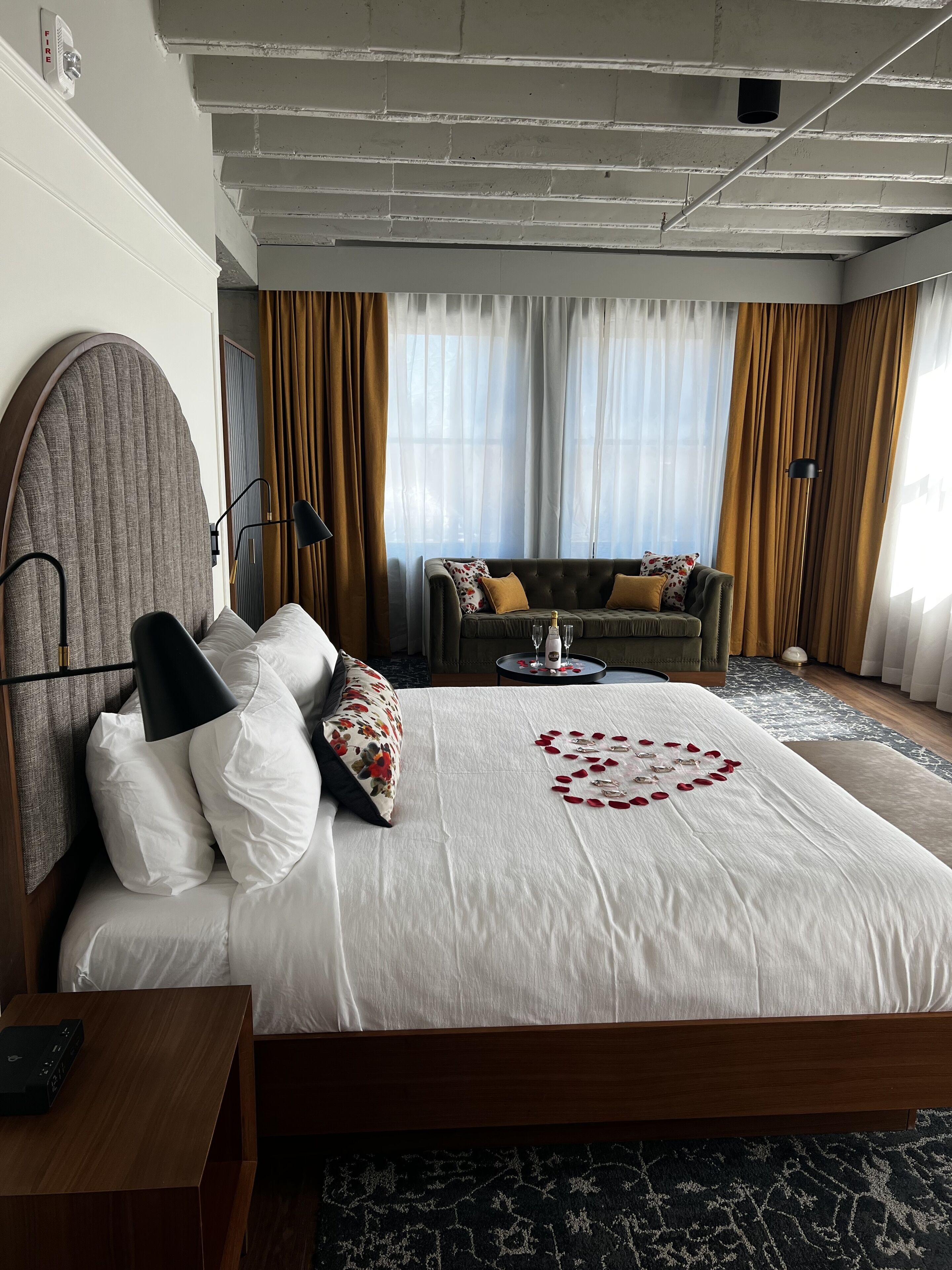 A hotel room with a large bed, a sofa, a coffee table, and a view of the outdoors.