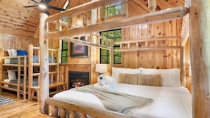 A log cabin bedroom with a bed, a fireplace, and wooden shelves.