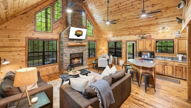 A spacious log cabin interior with a fireplace, wooden floors, a dining area, and a kitchen.