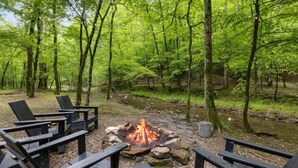 A forested campsite with a fire pit surrounded by wooden benches.