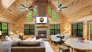 A cozy cabin interior with a stone fireplace, wooden walls, and a dining area.