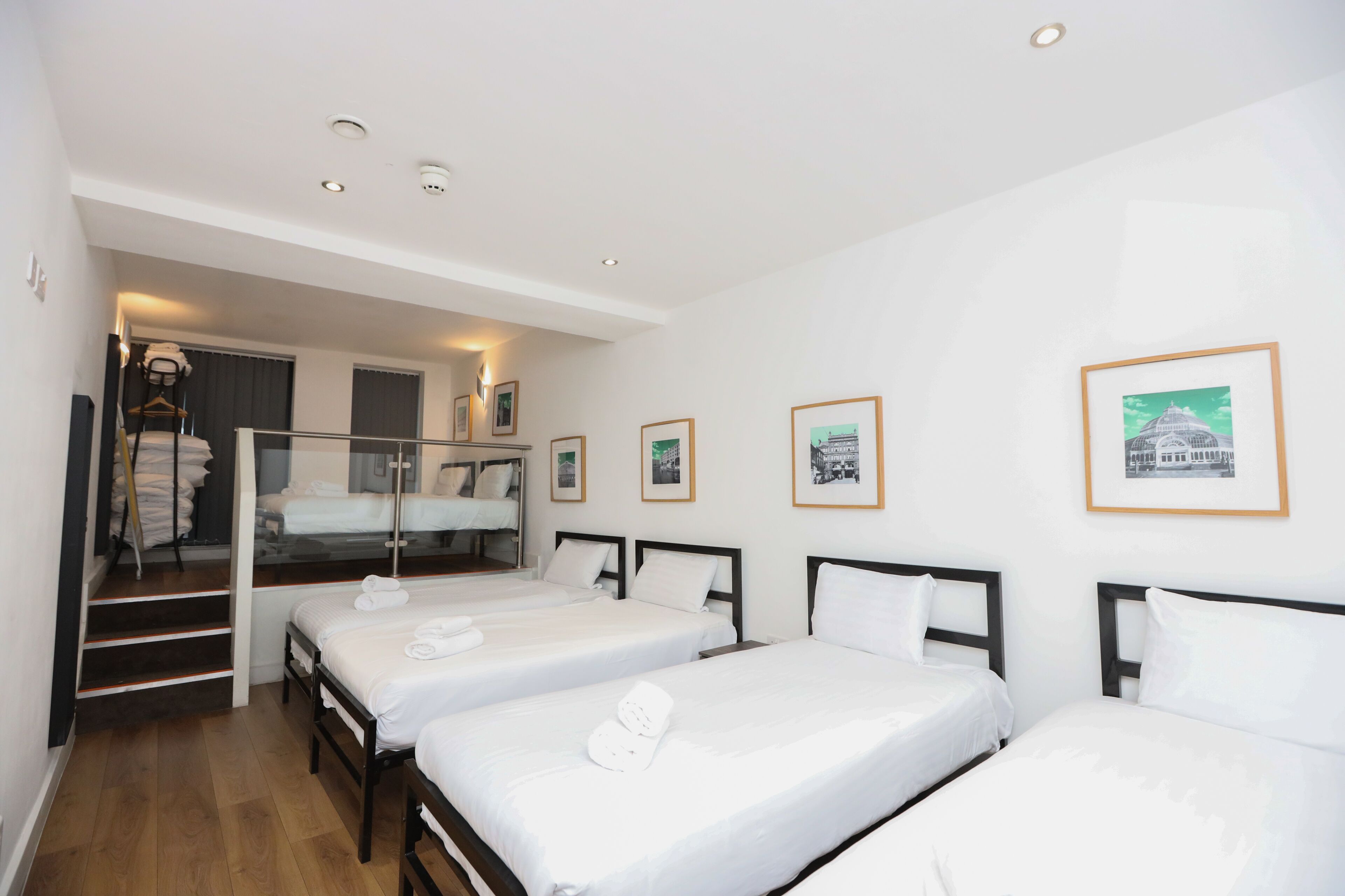 A hotel room with three single beds, a staircase, and framed pictures on the wall.