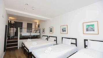 Habitación de hotel con tres camas individuales, una escalera y cuadros enmarcados en la pared.