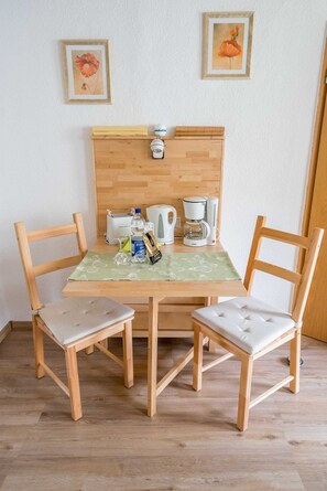 Une table à manger en bois, avec deux chaises, une machine à café, un grille-pain et une bouteille d’eau posés sur la table.