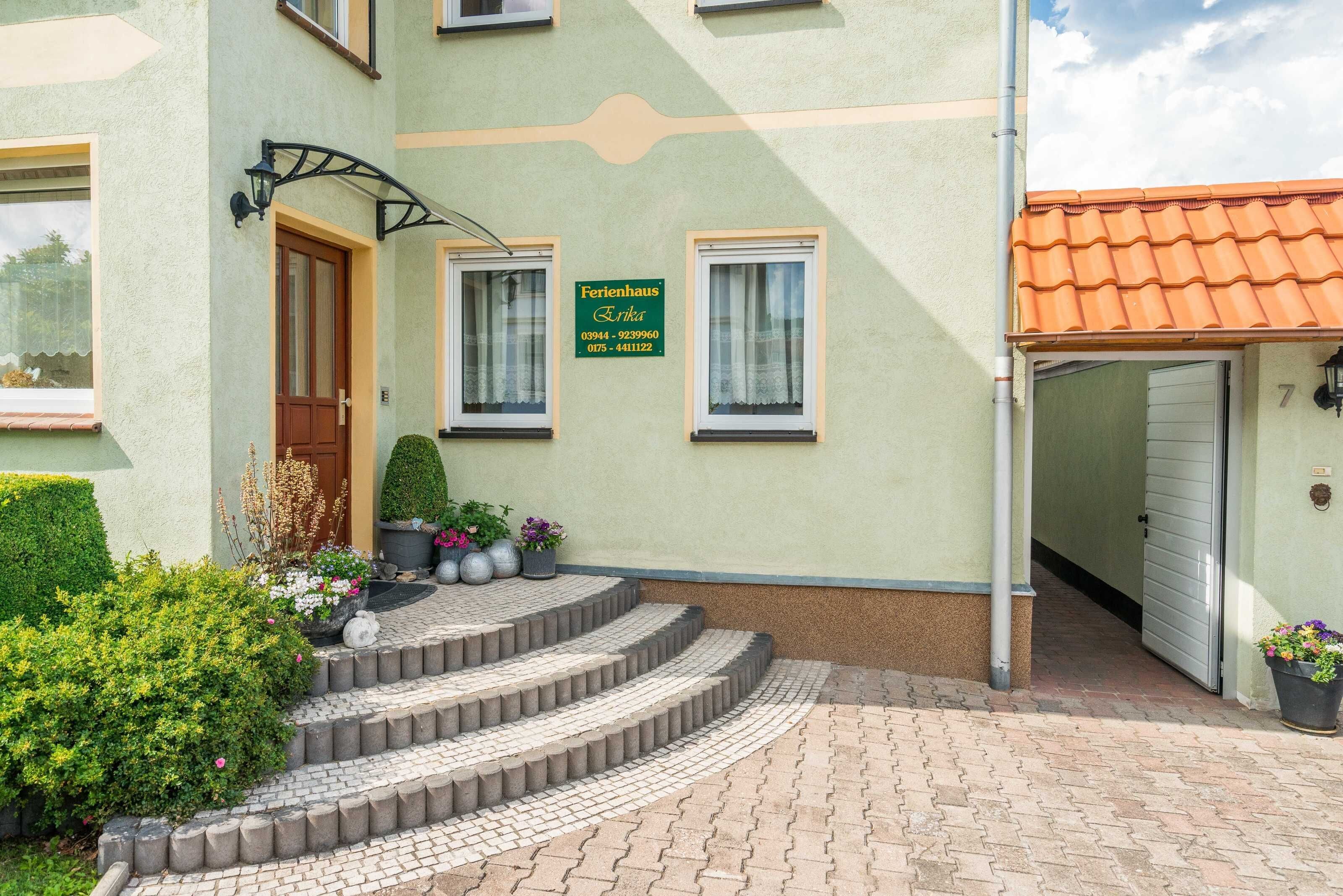 Ein Gebäude mit grüner Fassade, einem Schild mit der Aufschrift 'Ferienhaus Erika' und einer Treppe, die zum Eingang führt.