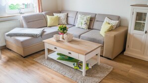 A living room with a sofa, a coffee table, a cabinet, and a window with a view. - Ferienwohnung Erika, Deutschland (Blankenburg (Harz))