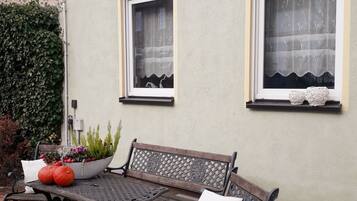 Eine Terrasse mit Tisch und zwei Bänken, einem Blumentopf und einer Wand mit zwei Fenstern.