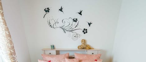 A neatly made bed with pink bedding, a decorative wall decal, and a window with curtains.