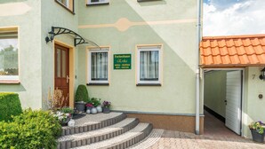 A building with a sign reading 'Ferienhaus Erika,' a set of steps leading to a door, and a small garden area with potted plants. - Ferienwohnung Erika, Deutschland (Blankenburg (Harz))