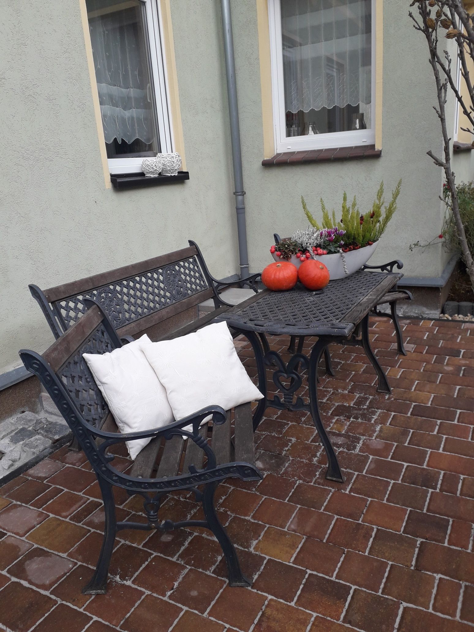 En uteplats med en bänk och ett bord, en krukväxt och ett fönster med en gardin.