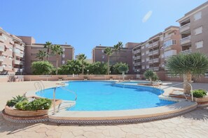 A swimming pool surrounded by a brick patio, with palm trees and a clear blue sky.