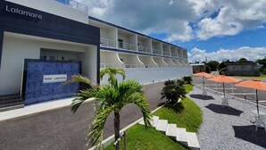 Un hôtel moderne, doté d’une enseigne, d’un espace extérieur abrité avec des parasols et offrant une vue sur un ciel dégagé.