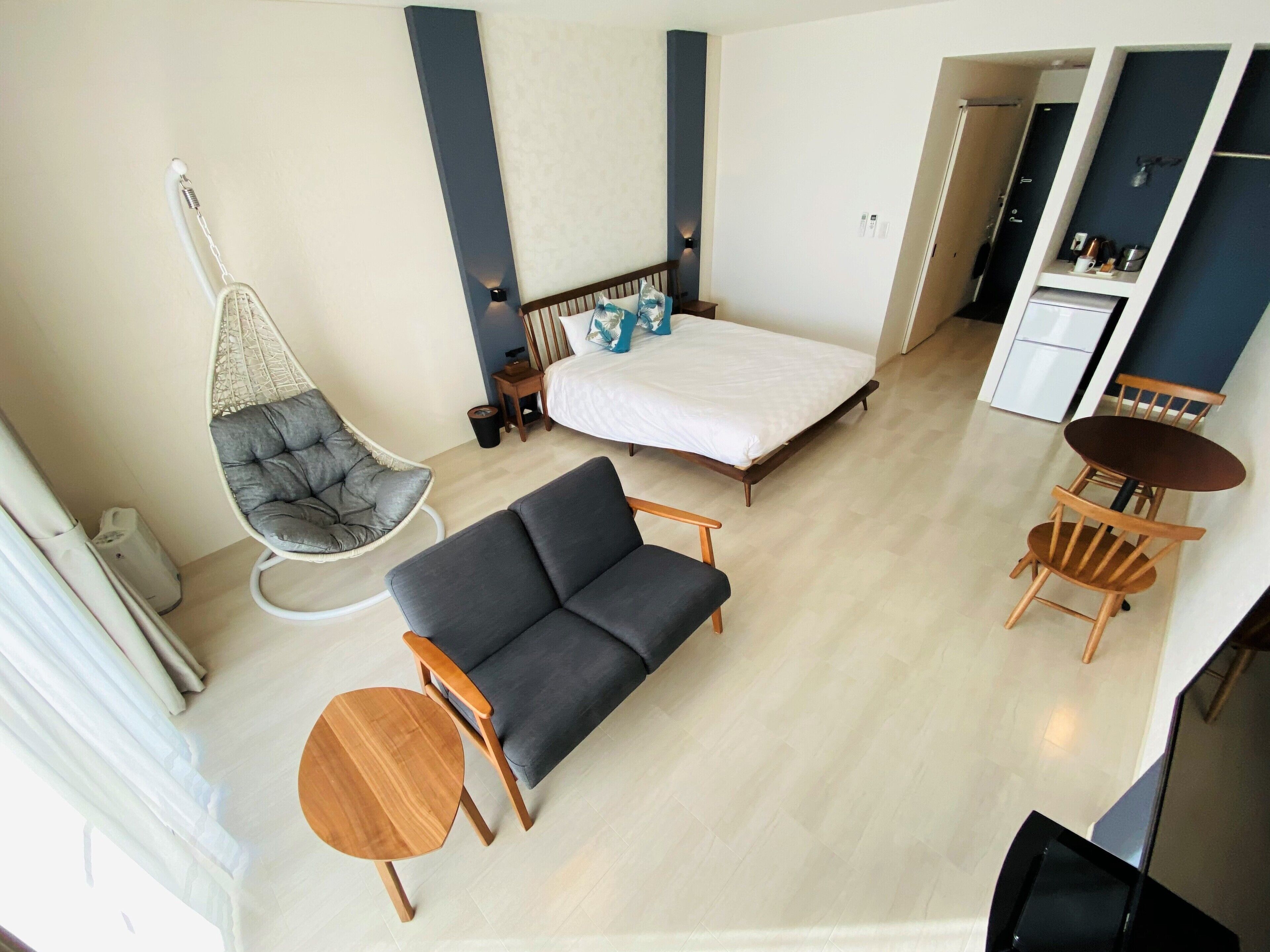 Une chambre d’hôtel moderne équipée d’un lit, d’un canapé, d’une chaise, d’une petite table et d’un fauteuil suspendu.