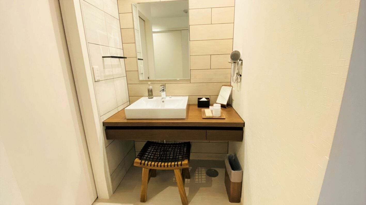 A bathroom with a white sink, a mirror, a towel rack, and a small stool.