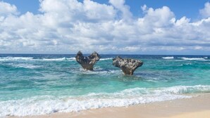 Une plage bordée d’eaux turquoise et transparentes, avec deux formations rocheuses imposantes qui émergent de la mer.
