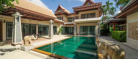 A modern villa with a swimming pool, stone elephant statues, and traditional architectural elements.