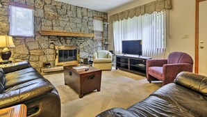 Una sala de estar con pared de piedra, chimenea, televisor y sofás de cuero.