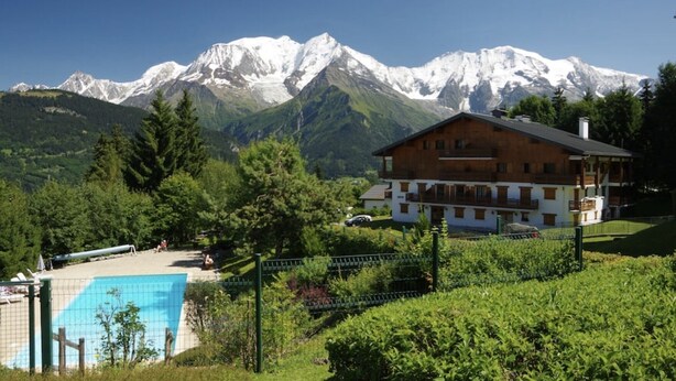 Un chalet en bois à deux étages, doté d’une piscine et offrant une vue sur les montagnes.