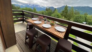 Une terrasse en bois avec une table dressée pour quatre personnes, offrant une vue sur un paysage montagneux.