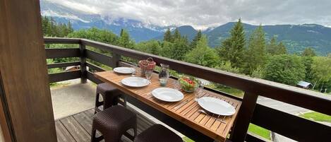 A wooden deck with a table set for four, overlooking a mountainous landscape.