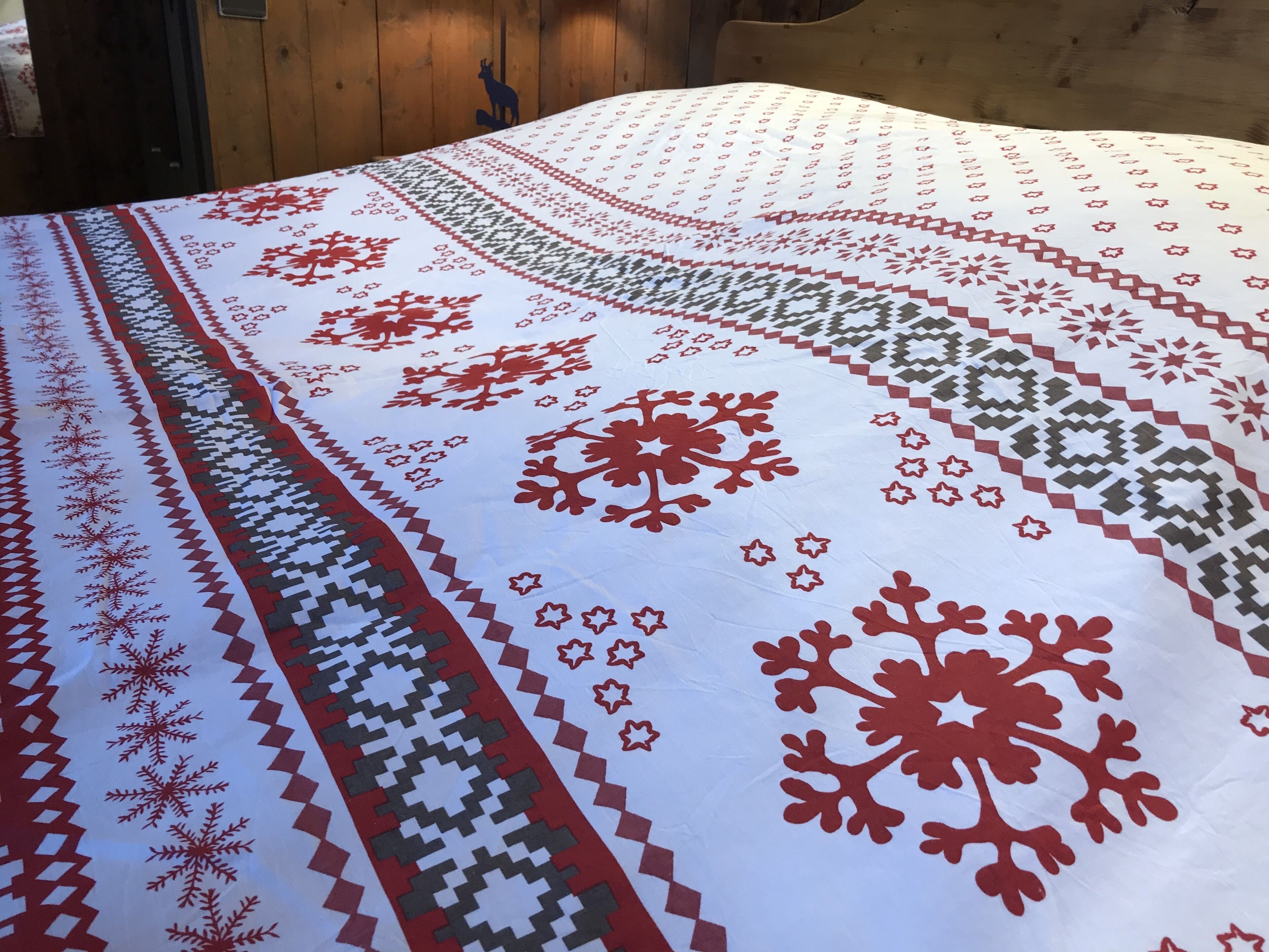 Een bed met een witte sprei met rode en groene sneeuwvlokmotieven.