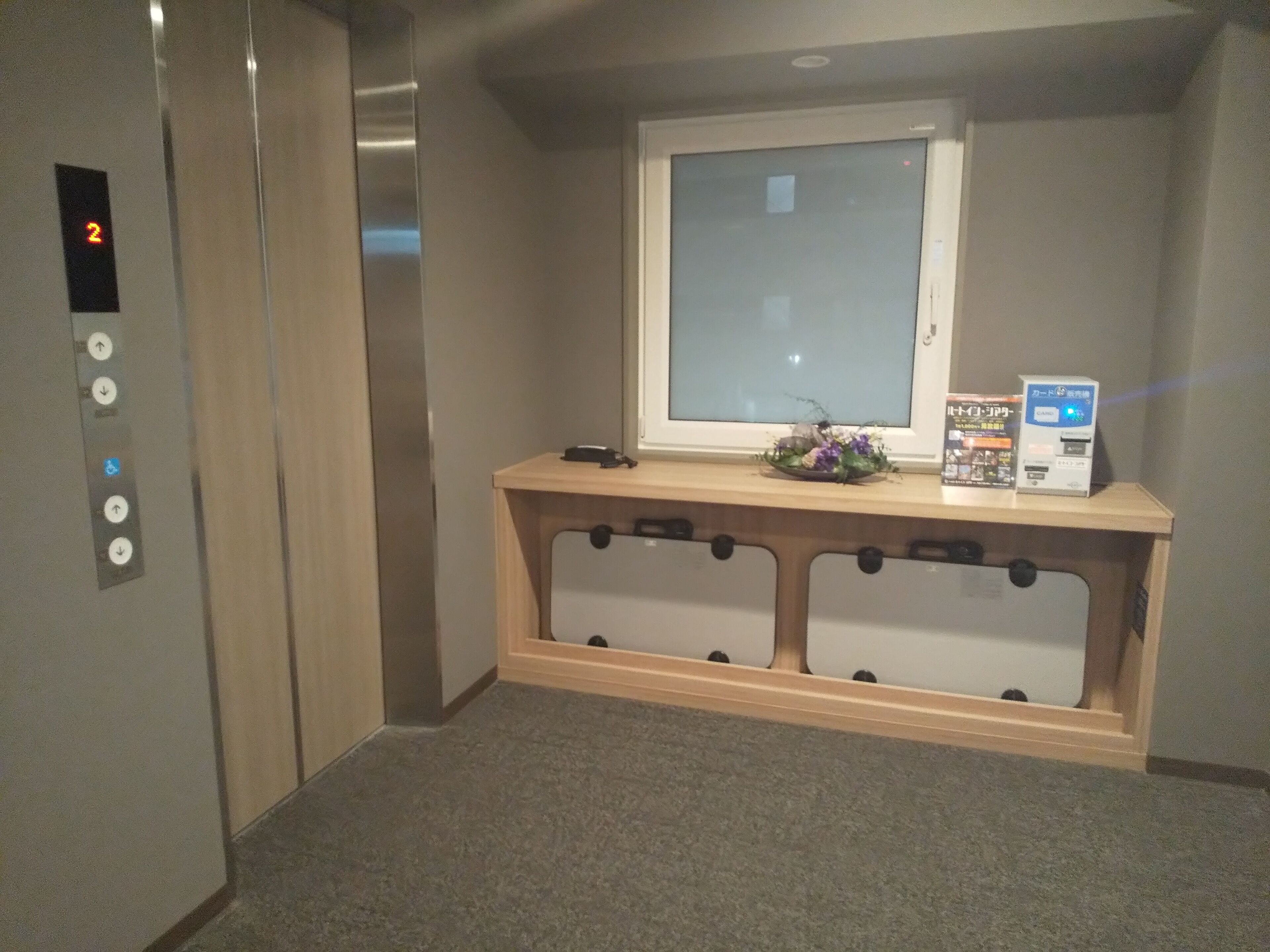 Een lift met een digitaal display waarop het cijfer 2 staat, een houten bedieningspaneel met een klein raam, en een kaartlezer.