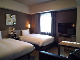 Habitación de hotel con dos camas, televisión, escritorio y ventana con cortinas.