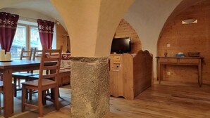 Ein rustikales Holzambiente mit einer Steinsäule, einem Holzesstisch, Stühlen und einem Fernseher in einer gemütlichen Einrichtung.