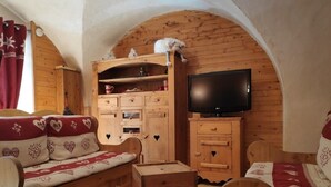 Ein gemütliches Zimmer mit einem Holzsofa, einem Holzschrank, einem Fernseher und einer kleinen Holzkiste.