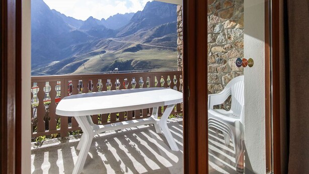 Un balcón con mesa y sillas blancas, con vistas a un paisaje montañoso.