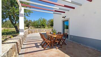 Une terrasse extérieure avec une table et des chaises, un mur en pierre et une vue sur les arbres et le ciel.