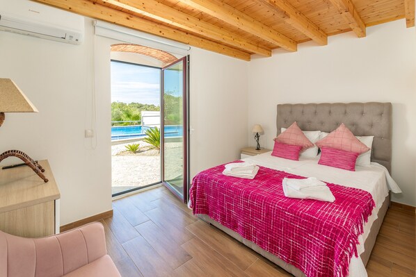 A bedroom with a bed, a desk, a chair, a window with a view of a pool and greenery, and a wooden ceiling. - Charming "Villa Rodrigues" with Air Conditioning, Wi-Fi, Pool & Garden (Boliqueime)
