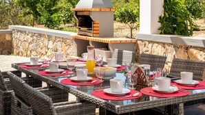 An outdoor dining area with wicker chairs, a stone wall, and a brick oven. - Charming "Villa Rodrigues" with Air Conditioning, Wi-Fi, Pool & Garden (Boliqueime)
