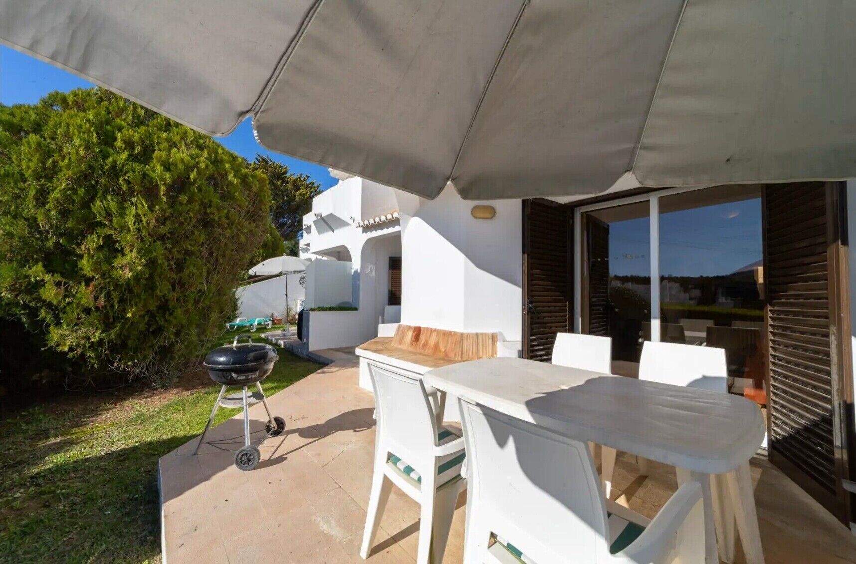 An outdoor patio with a table and chairs, a grill, and a covered area.
